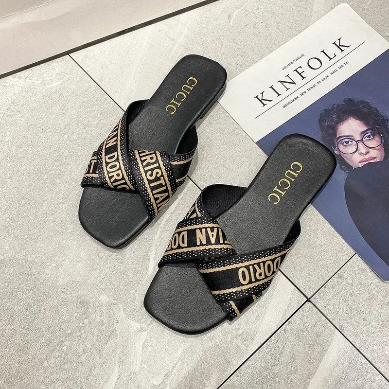 Black women's summer slippers with stylish branded straps on tiled floor next to a magazine