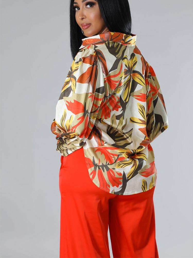 Floral printed lantern sleeve women's shirt paired with red pants on model against gray background