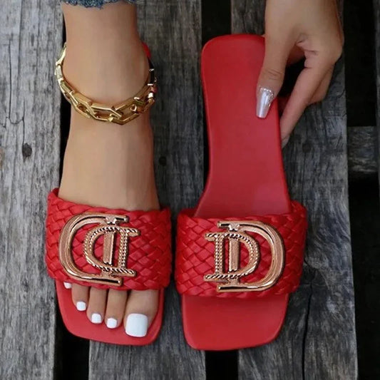Women's luxury slippers in red with gold decorative buckle and braided strap, worn with gold anklet and white nail polish.