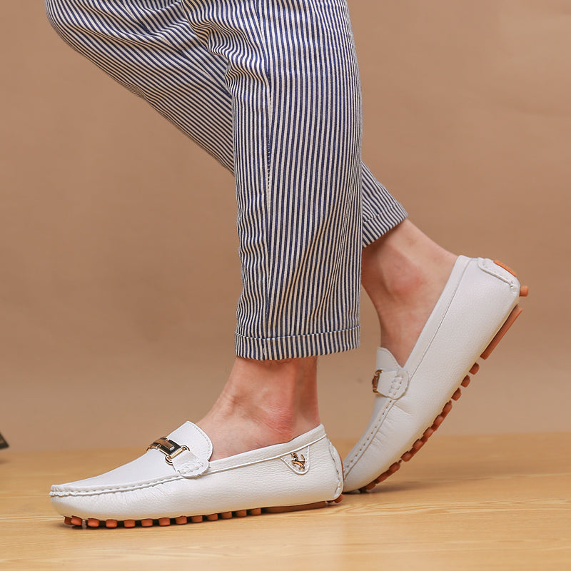 White men's leather loafers with brown sole and gold buckle detail worn with striped pants