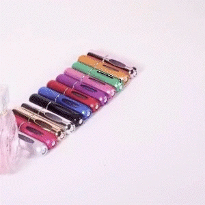 Colorful small perfume spray bottles with aluminum exterior and clear glass reservoirs arranged in a row on a light surface