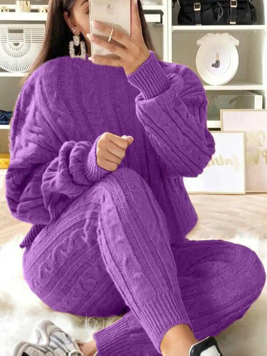 Woman wearing a purple women's long sleeve knitted sweater and matching pants sitting indoors taking a mirror selfie