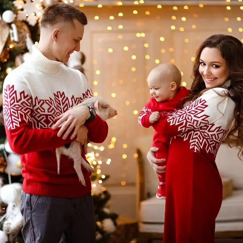 Family wearing red and white Christmas family matching sweaters with snowflake patterns, celebrating holiday season indoors with festive decorations.