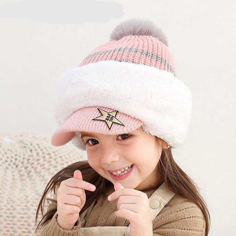 Smiling child wearing a pink and white warm winter hat with a pom-pom and visor, cozy winter accessory for kids