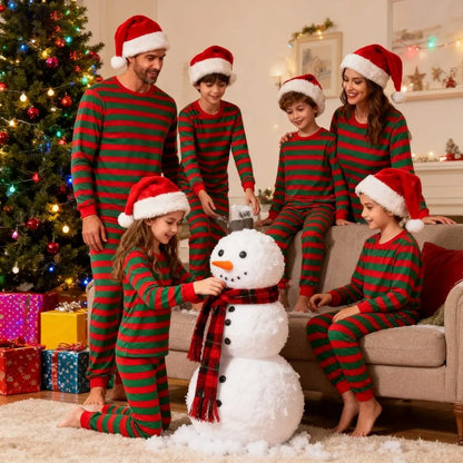 family Christmas pajamas matching red and green striped sets with Santa hats around snowman indoors