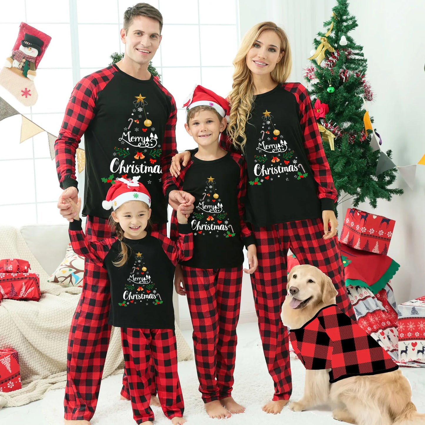 Family wearing matching Christmas pajamas with black tops and red plaid pants alongside a dog in a matching festive outfit near a decorated Christmas tree