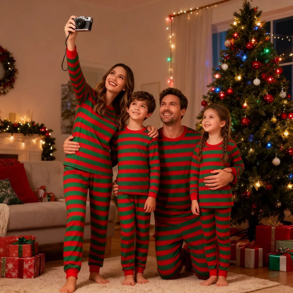 Family Christmas pajamas in red and green stripes worn by smiling family taking selfie near decorated Christmas tree and gifts