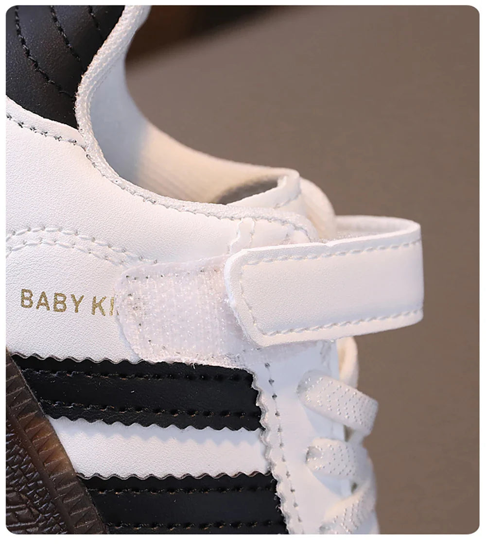 Close-up of white and black unisex sneakers for kids with velcro strap and laces